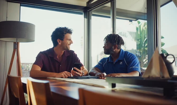 Paquete de ADT en un estante Un profesional de ADT se sienta en una mesa con un propietario, información profesional sobre la instalación en un dispositivo móvil.